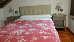 Un dormitorio con una cama, dos mesitas de noche, una lámpara y una estantería en la pared.