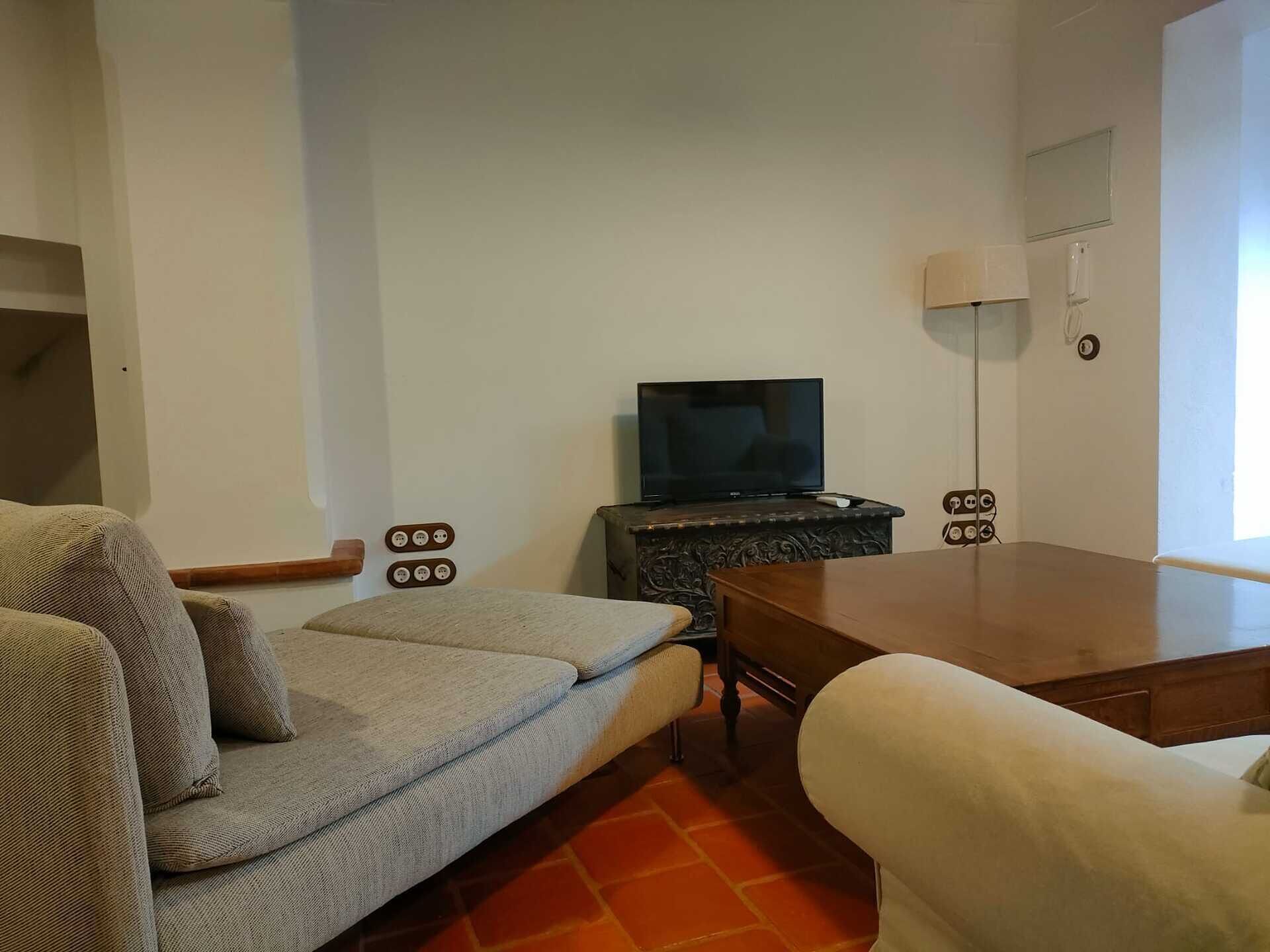 Ein Wohnzimmer mit einer Couch, einem Couchtisch, einem Fernseher auf einem Schrank und einer Lampe.