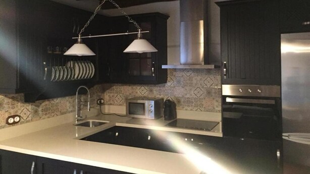 Una cocina moderna con armarios oscuros, un refrigerador de acero inoxidable, horno empotrado, microondas y una pileta doble.