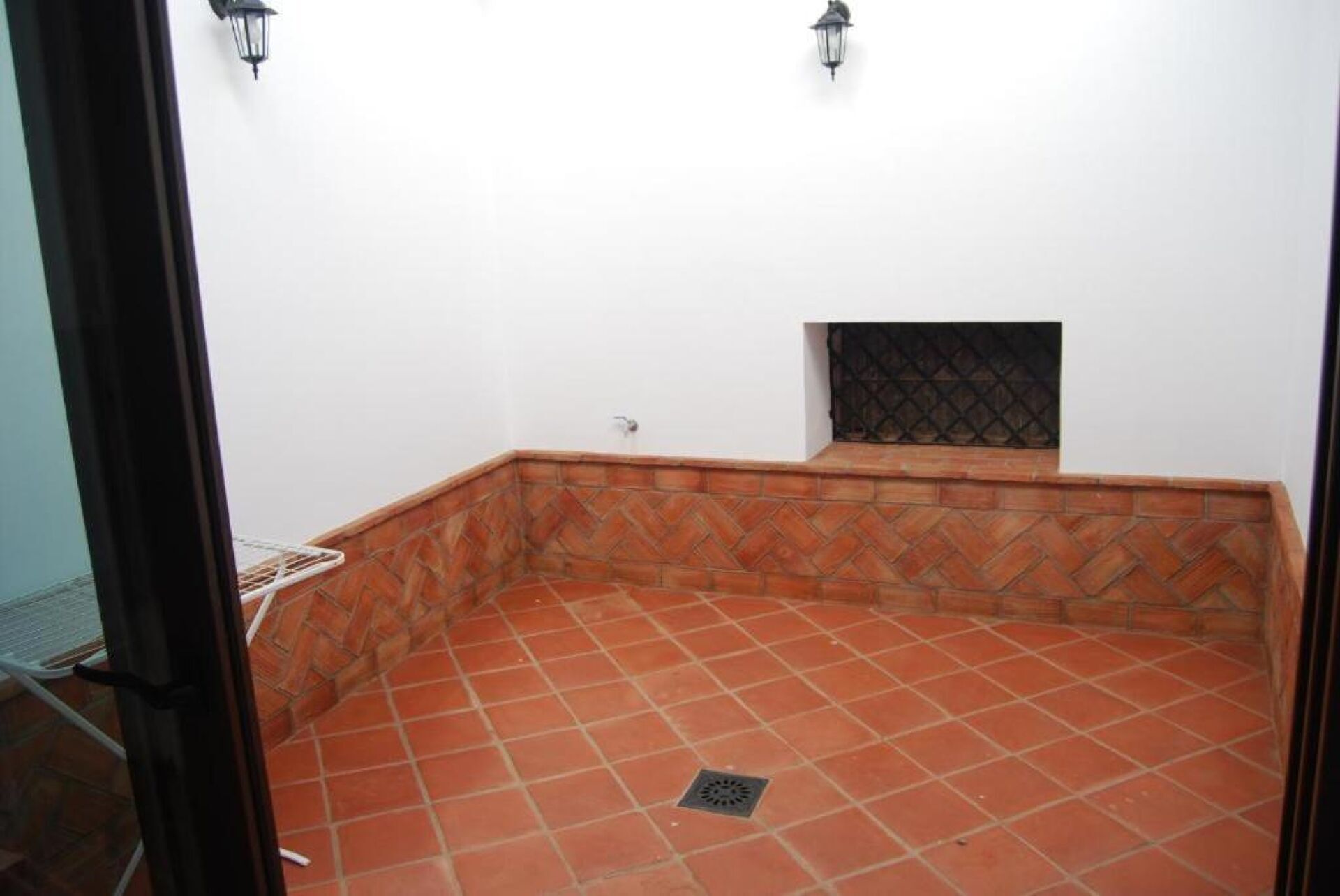 A room with a tiled floor, a small window with a metal grille, and two wall-mounted light fixtures.