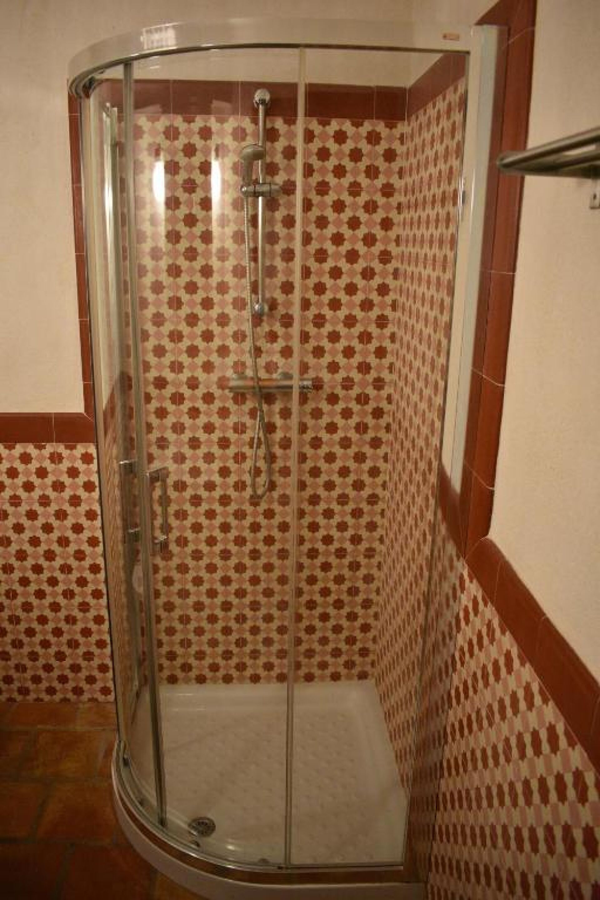A shower with a glass door and a tiled wall with a geometric pattern.