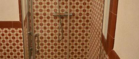 A shower with a glass door and a tiled wall with a geometric pattern.