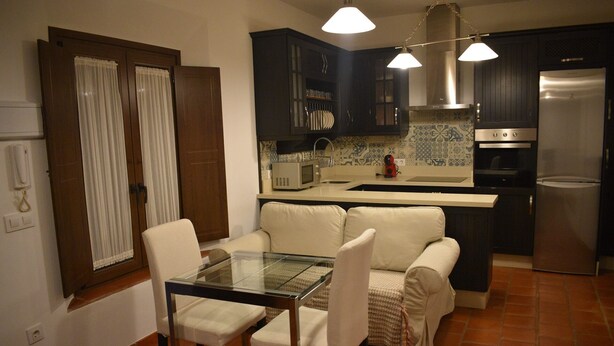 A compact kitchen with dark cabinets, a refrigerator, a microwave, and a glass dining table with chairs. - Bodeguetas 1 bedroom with patio pets welcome (Constantina)