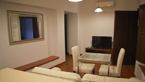 A small, well-lit room with a sofa, a TV on a stand, and a mirror on the wall. - Bodeguetas 1 bedroom with patio pets welcome (Constantina)