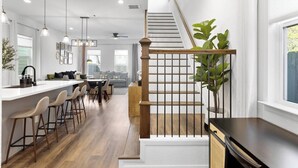 A modern kitchen with a central island, bar stools, pendant lighting, and a staircase with a wooden railing. - Houston Family Retreat | Sleeps 10 | Near NRG (Houston)