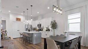 A modern kitchen with white cabinetry, a central island with bar stools, and pendant lighting. - Houston Family Retreat | Sleeps 10 | Near NRG (Houston)