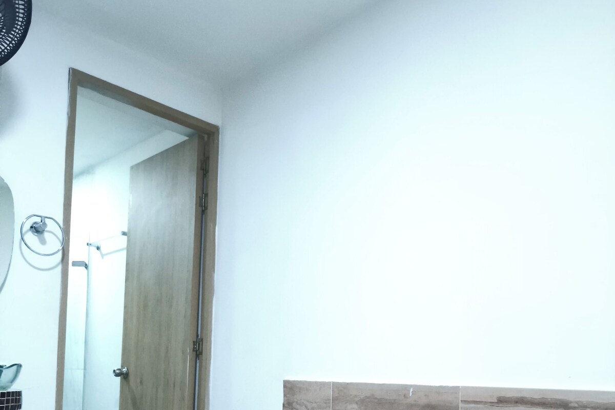 Ein Schlafzimmer mit Holztür, einem Bett mit floralem Bettzeug und einem an der Wand befestigten Ventilator.