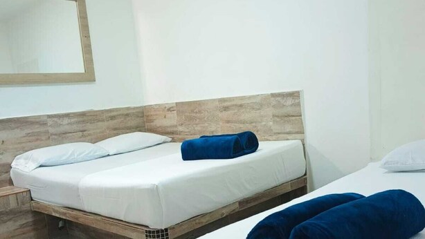 A hotel room with two beds, each with white linens and a wooden headboard. There are blue towels on the beds. - Hotel Casa Girardot (Medellin)