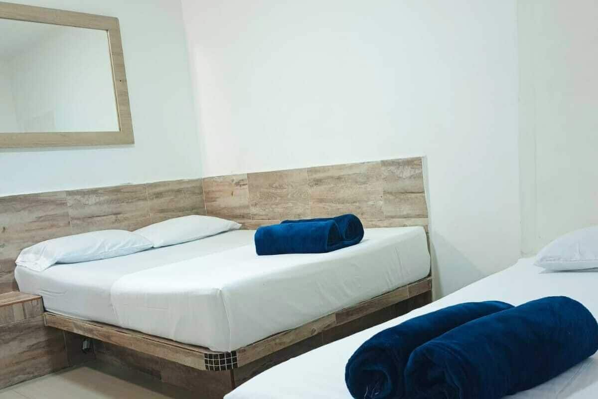 Ein Hotelzimmer mit zwei Betten, jeweils mit weißen Leinen und einem Holz-Kopfteil. Auf den Betten liegen blaue Handtücher.