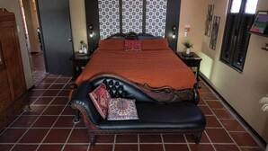 Une chambre à coucher avec un grand lit, une armoire en bois, une petite table avec une plante et une fenêtre avec des stores.