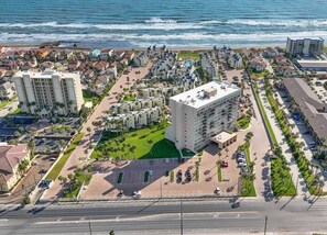 An aerial view of a coastal hotel with multiple buildings, a central courtyard, and a beachfront.