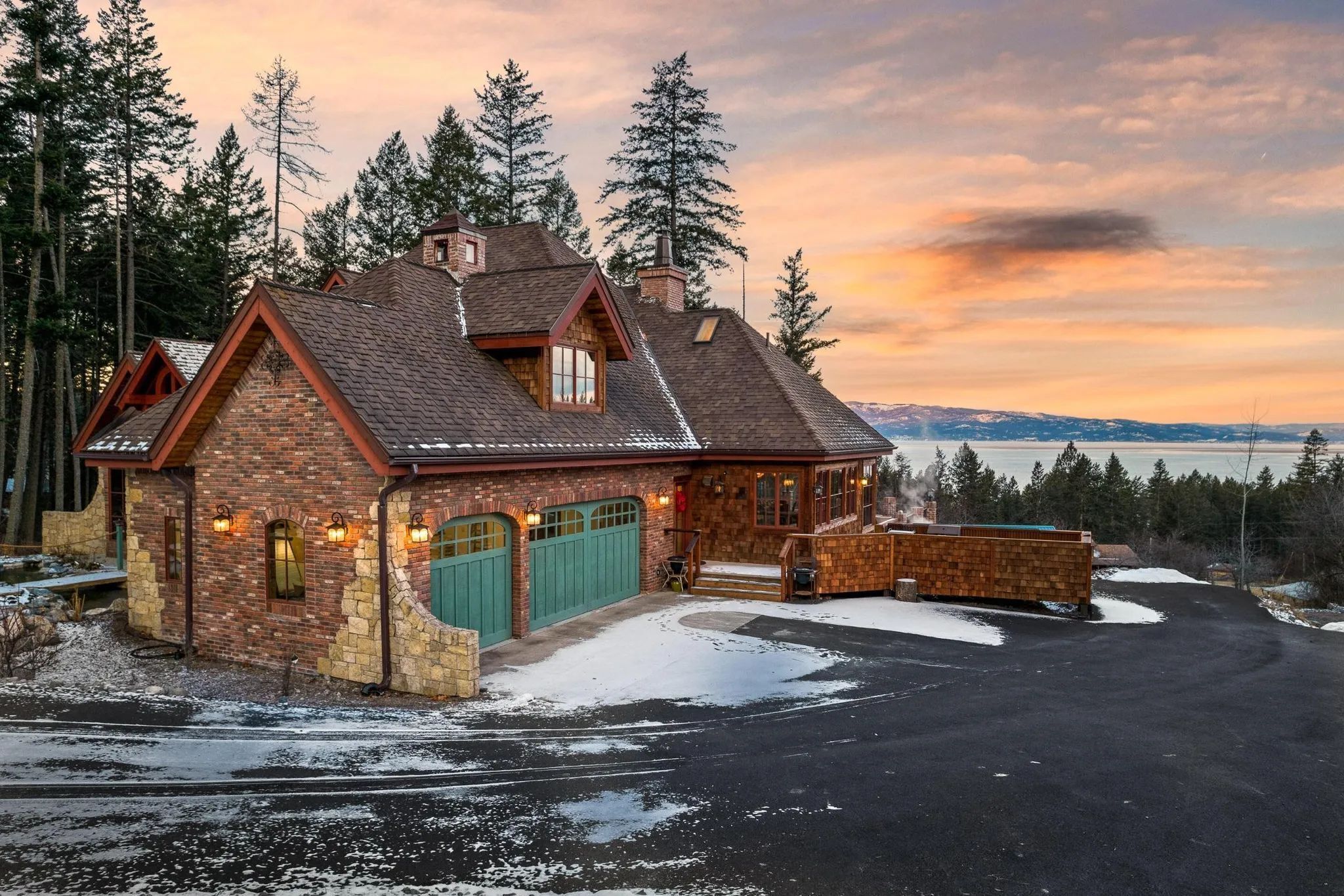 Exterior view of the house and driveway at sunset, with a deck overlooking the water.