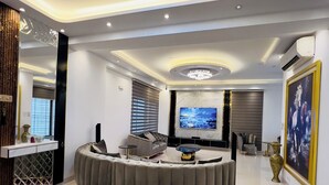 A modern living room with a curved grey sofa, a flat-screen TV, and a decorative vase. - 10 minutes from airport, Elegant Villa in modern, secure city Basundhara R/S. (Bashundhara R/S)