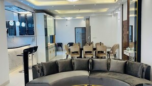 A modern living room with a curved sectional sofa, a black coffee table, and a dining area with chairs and a table. - 10 minutes from airport, Elegant Villa in modern, secure city Basundhara R/S. (Bashundhara R/S)