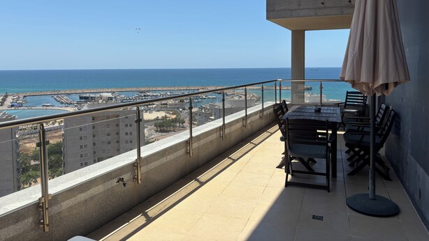 A balcony with a view of the sea, a table with chairs, and an umbrella. - MARINA LUXURY APARTMENT WITH TERRACE EXCEPTIONAL SEA VIEW BEACH 3 MN (Ashdod)