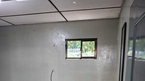 A small, simple room with a bed, a small window, a trash can, and a door. - Spacious apartment (ss)