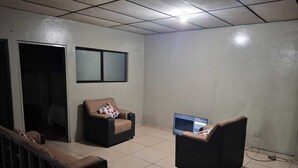 A room with a sofa, a chair, a television, and a window. - Spacious apartment (ss)