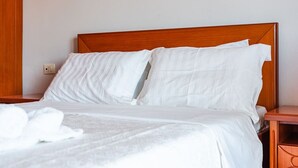 Un lit bien fait, avec du linge de lit blanc et des oreillers, une tête de lit en bois et une table de chevet en bois avec une lampe.