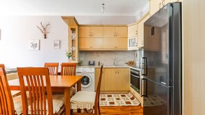 Une cuisine compacte avec des meubles en bois, un lave-linge, un réfrigérateur et une table à manger avec des chaises.