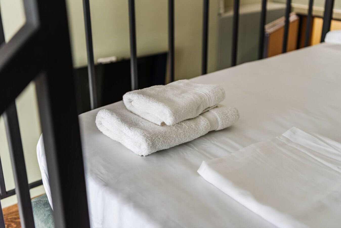 Una cama bien hecha con sábanas blancas y dos toallas dobladas a un lado.