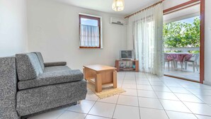 A living room with a grey sofa, a wooden coffee table, a TV, and a balcony with a table and chairs. - Holiday apartment mit Balkon (Baška)