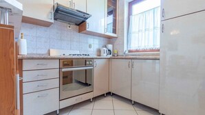 A kitchen with light-colored cabinets, a built-in oven, a stove, and a window with a curtain. - Holiday apartment mit Balkon (Baška)