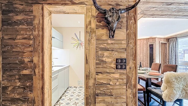 A rustic interior with wooden walls, a dining area with a table and chairs, and a bull skull decoration.