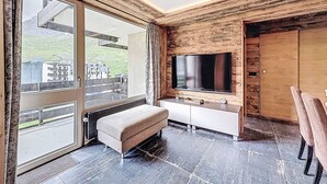 A modern living room with a large TV, a bench, and a sliding glass door leading to an outdoor area.