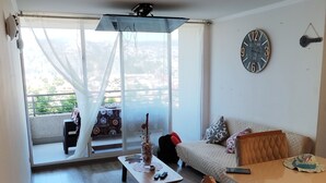 Ett rymligt vardagsrum med trägolv, en soffa, ett soffbord och ett matbord. Ett stort fönster ger utsikt över omgivningen.