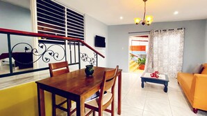 A dining area with a wooden table and chairs, a staircase with a railing, and a living room with a sofa and a small table.