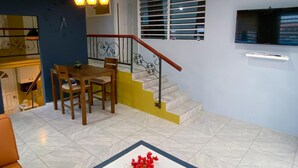 A dining area with a table and chairs, a staircase with a railing, and a television mounted on the wall.