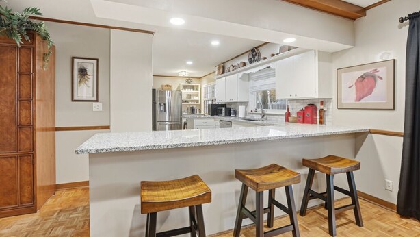 A modern kitchen with white cabinets, a granite countertop, and three wooden stools. - Stunning 4-Bedroom Home with Outdoor Pool & A/C in Ponca City (Ponca City)