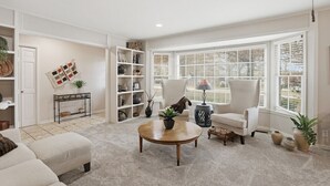 A living room with a large window, a white armchair, a coffee table, and a bookshelf. - Stunning 4-Bedroom Home with Outdoor Pool & A/C in Ponca City (Ponca City)