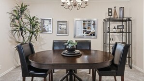 A dining room with a round table, black chairs, a chandelier, framed pictures, and a plant. - Stunning 4-Bedroom Home with Outdoor Pool & A/C in Ponca City (Ponca City)