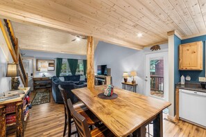 A spacious living area with a wooden dining table, a sofa, and a television in the background. - Maggie Valley, Tenn, hiking, skiing, tubing, dog-friendly, cozy cabin (Maggie Valley)