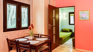 A wooden dining table with chairs and a vase of flowers, a bed with a green blanket, and a door leading to a room with a window. - 1 bedroom gorgeous home in Lazy (Lazy)
