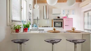 Une cuisine moderne dotée d’un îlot central, de tabourets de bar, d’un réfrigérateur rose et de luminaires suspendus.