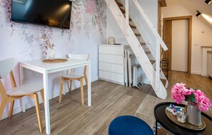 A modern living room with a white table, two chairs, a TV mounted on the wall, a staircase, and a small table with a vase of flowers. - 1 bedroom pet friendly apartment in Nowecin (Nowecin)