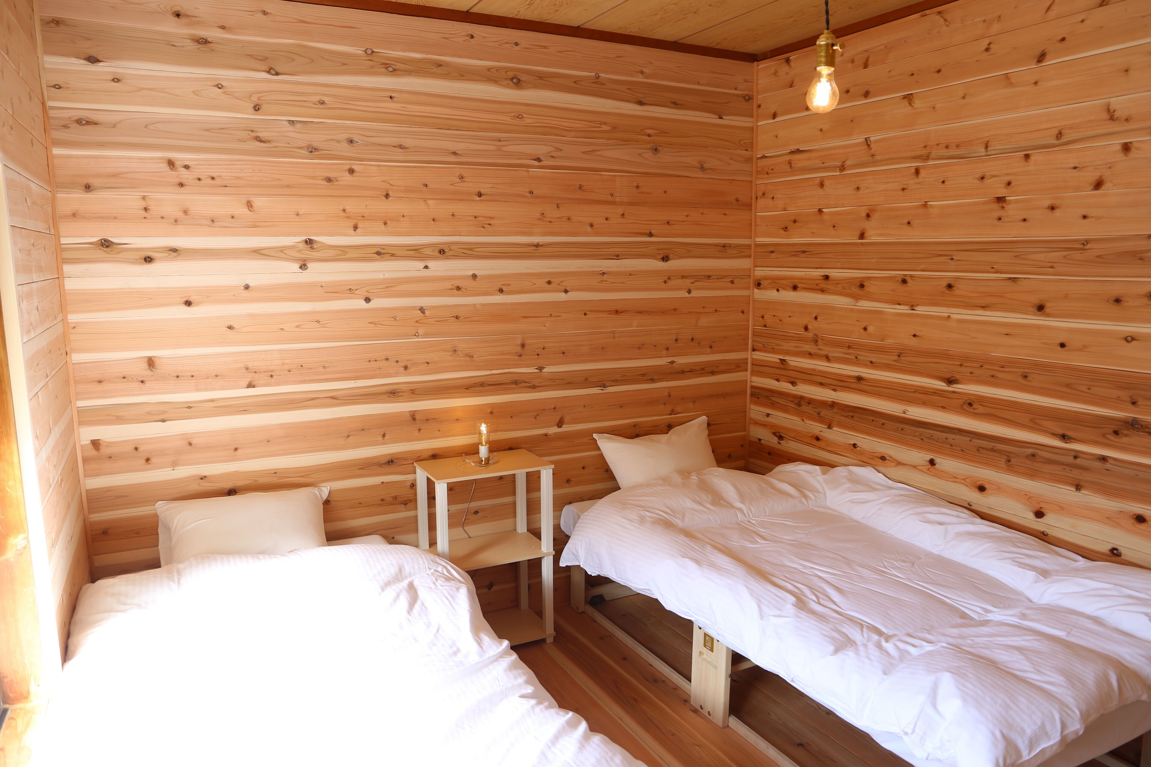 A wooden cabin room with two beds, a small table, and a hanging light fixture.