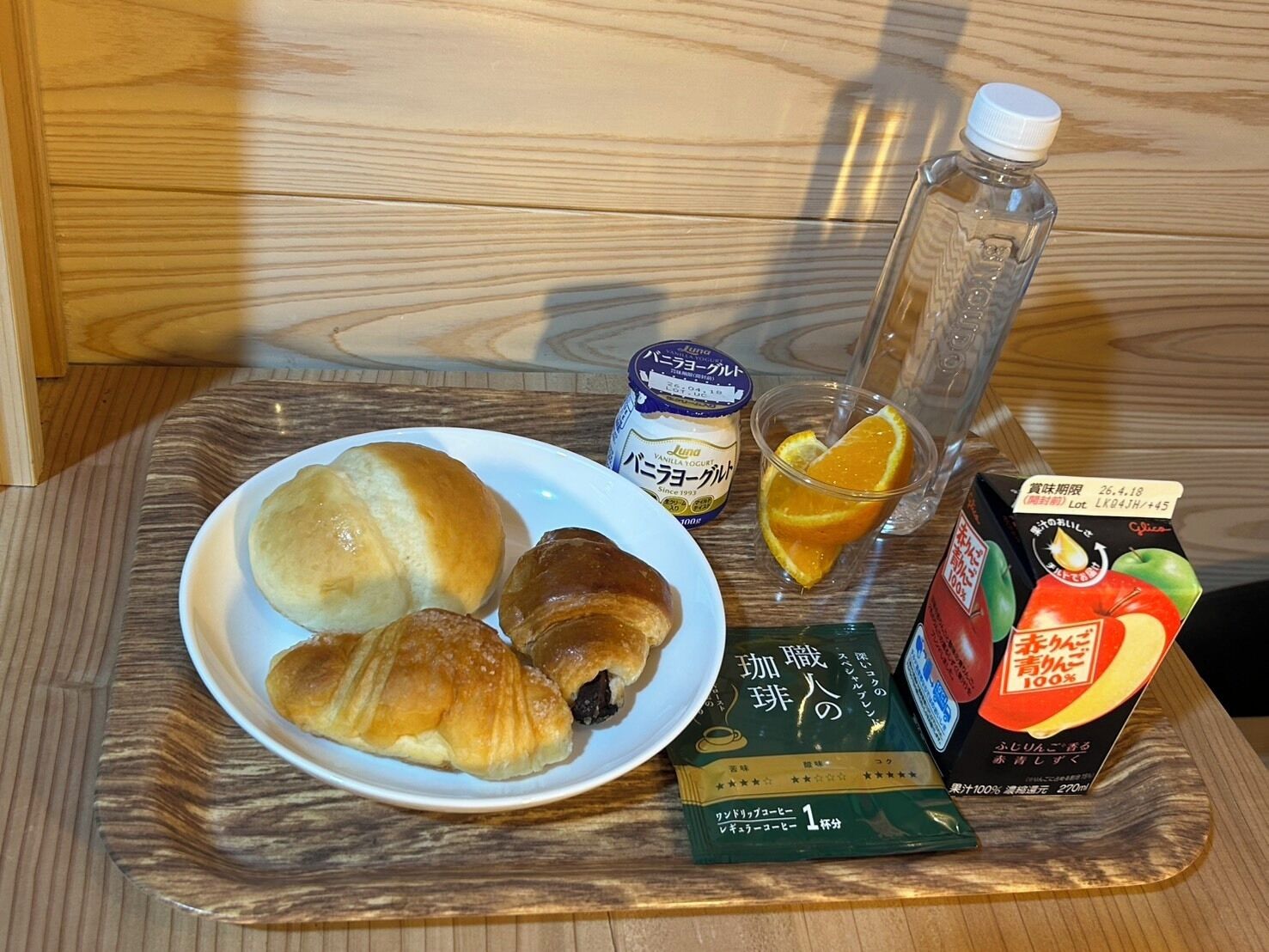 A tray with croissants, a glass of orange juice, a bottle of water, a container of yogurt, and a pack of instant coffee.