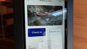 A digital kiosk with a screen displaying a scenic image of a river and a kayak, along with options for 'Check In' and 'Check Out.' - Riviera Iya Valley (Miyoshi)