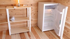 A compact room with a wooden interior, a small table with a candle, and a white refrigerator. - Riviera Iya Valley (Miyoshi)