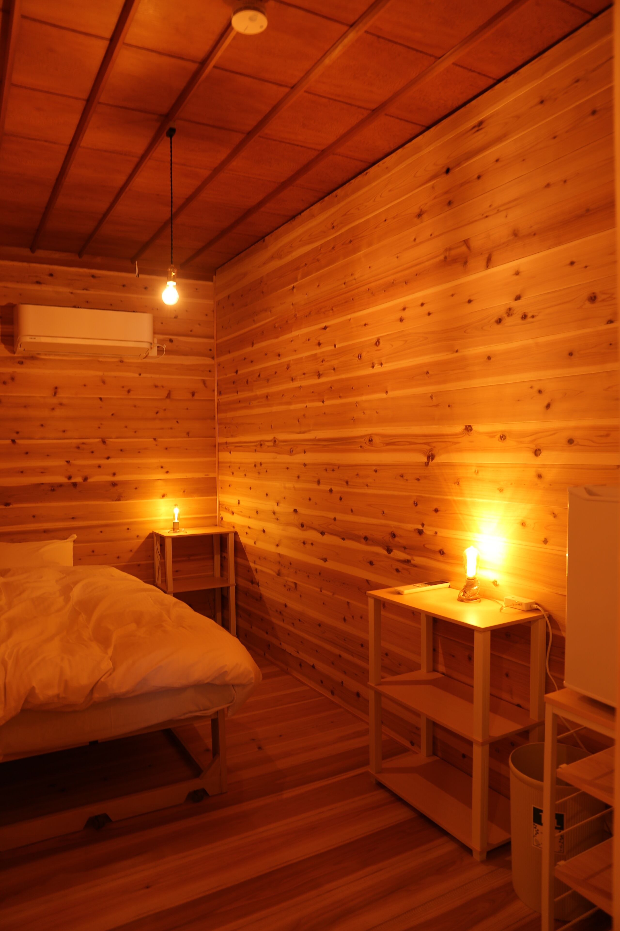 Habitación de cabaña de madera con una cama, dos mesitas de noche con lámparas y un equipo de aire acondicionado blanco.