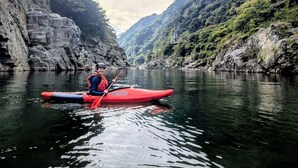 A kayaker in a red kayak on a calm river surrounded by rocky cliffs. - Riviera Iya Valley (Miyoshi)