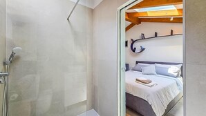 Et moderne badeværelse med et glasbadeværelse og et synligt soveværelse med seng, puder og en bog.