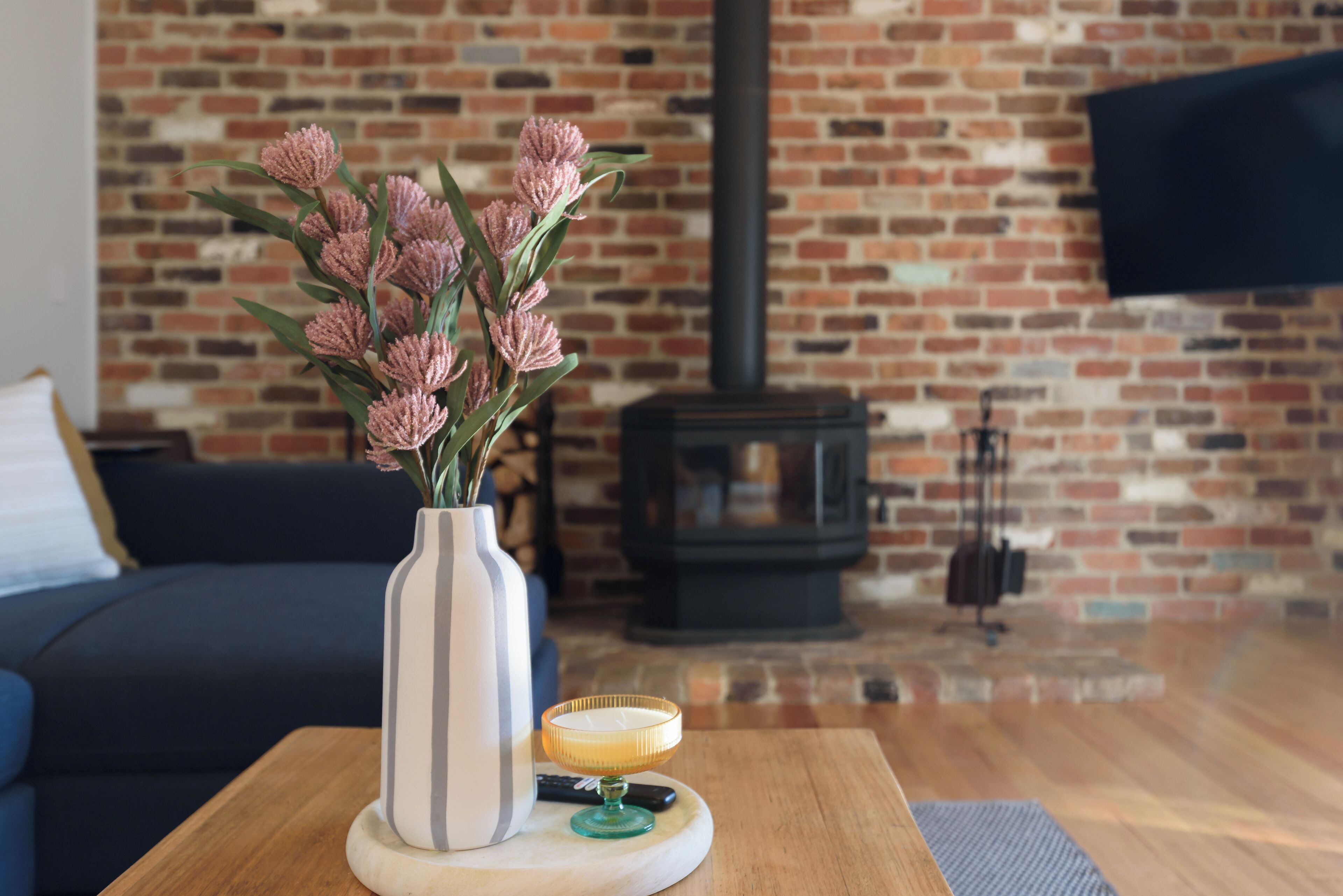 Ein Wohnzimmer mit Backsteinwand, einer Couch, einem Couchtisch mit Blumenvase und einem Kamin.