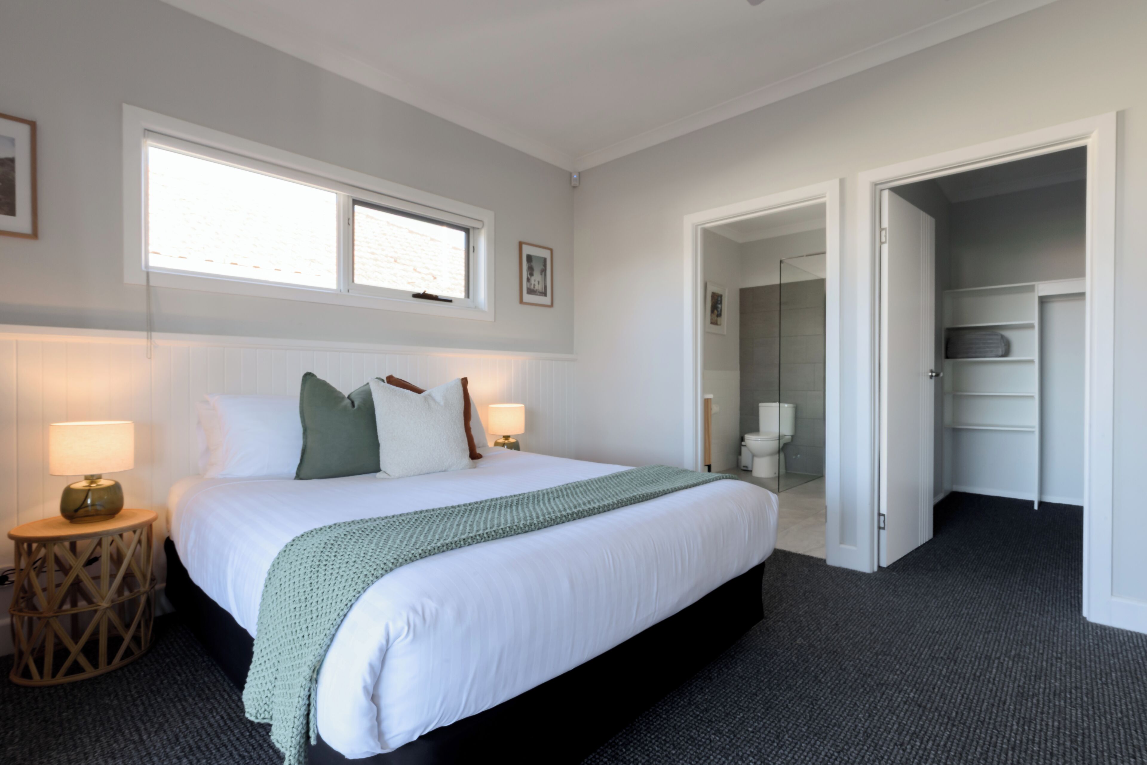 A bedroom with a large bed, two bedside lamps, a window, and a door leading to a bathroom.
