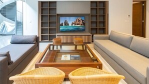 A modern living room with a large flat-screen TV, a sofa, two wicker chairs, and a coffee table with a glass top.