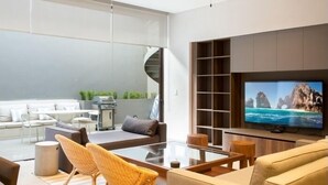 A modern living room with a glass coffee table, wicker chairs, a sofa, and a television on a wooden stand.