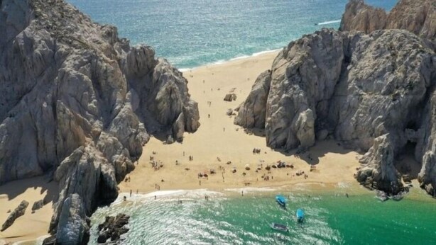 A beach with rocky cliffs, clear blue water, and a sandy shore.